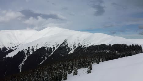 snow-covered papusa peak with cloud-draped iezer-papusa mountains in romania, evergreen contrast