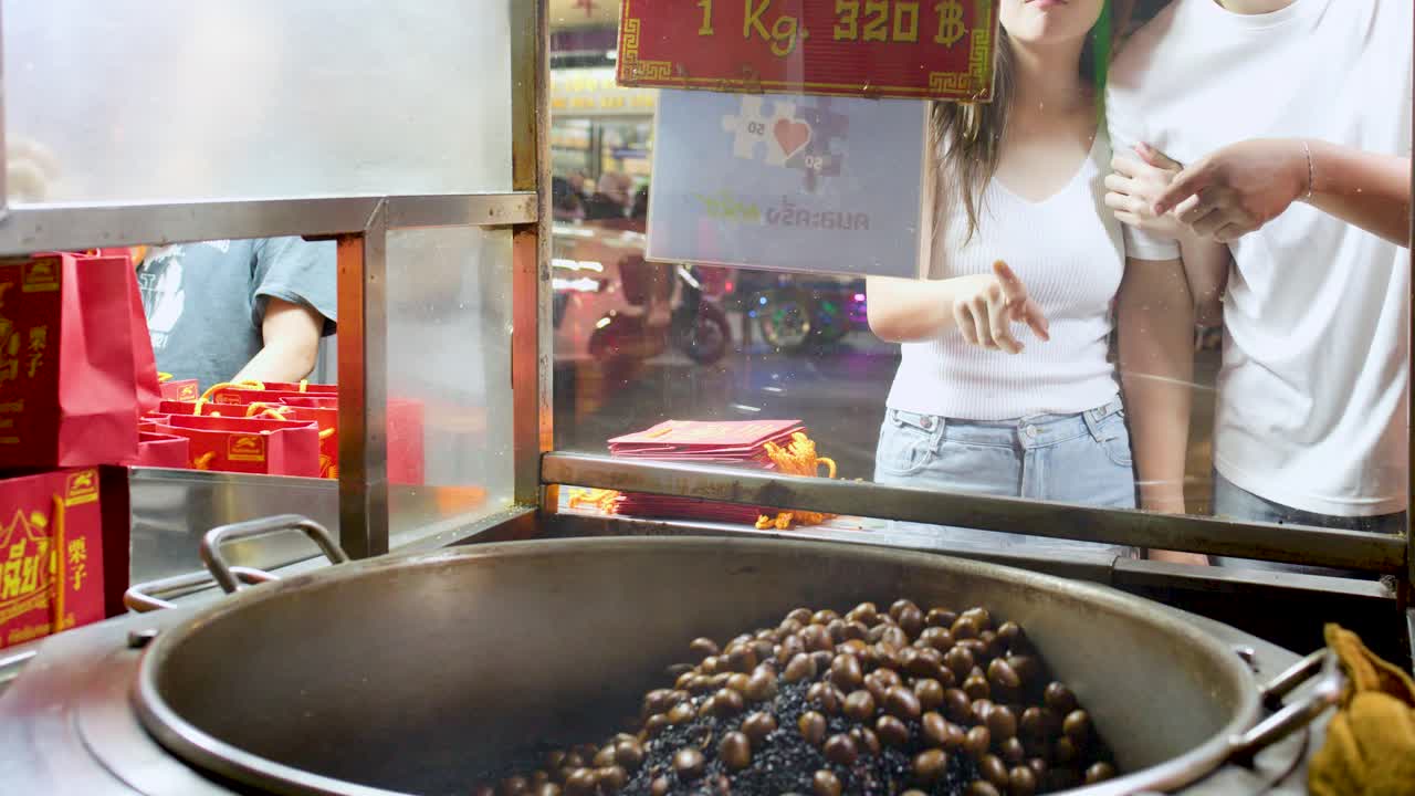 Young couple interacts and purchases roasted chestnuts at vibrant night street food market stall