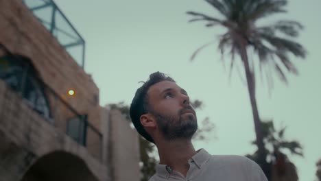 Retrato-De-Hombre-Elegante-Y-Guapo-Mirando-Al-Cielo-Con-Fondo-De-Calle-Tropical