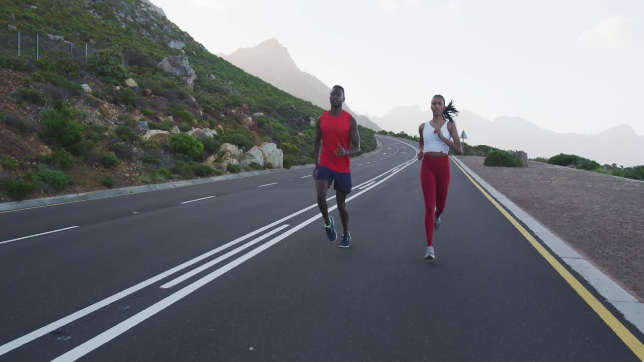 Diverse fit couple exercising running on a country road near mountains