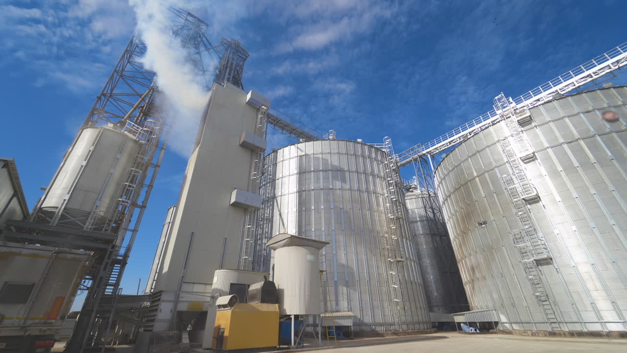 Agricultural Silos. Metal grain facility with silos. Storage and drying of grains, wheat, corn, soy, sunflower against the blue sky with white clouds