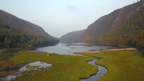 Aerial-shot-following-river-with-Glendalough-Upper-Lake-in-the-background-in-Wicklow-National-Park,-Ireland