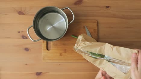 top down view of hands emptying a bag of green beans and cutting them on a bamboo cutting board, and putting them in a pan of water