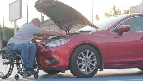 hombre con discapacidad en silla de ruedas revisa el motor de su coche en el estacionamiento