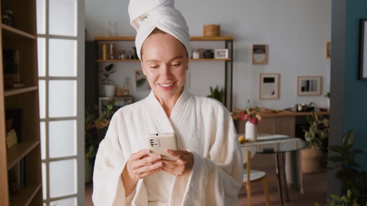 Donna in accappatoio che usa uno smartphone a casa