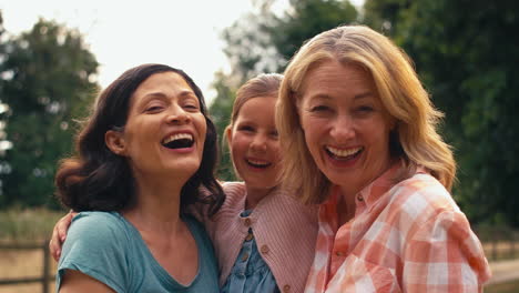 portrait of same sex family with two loving mature mums hugging daughter on walk in countryside