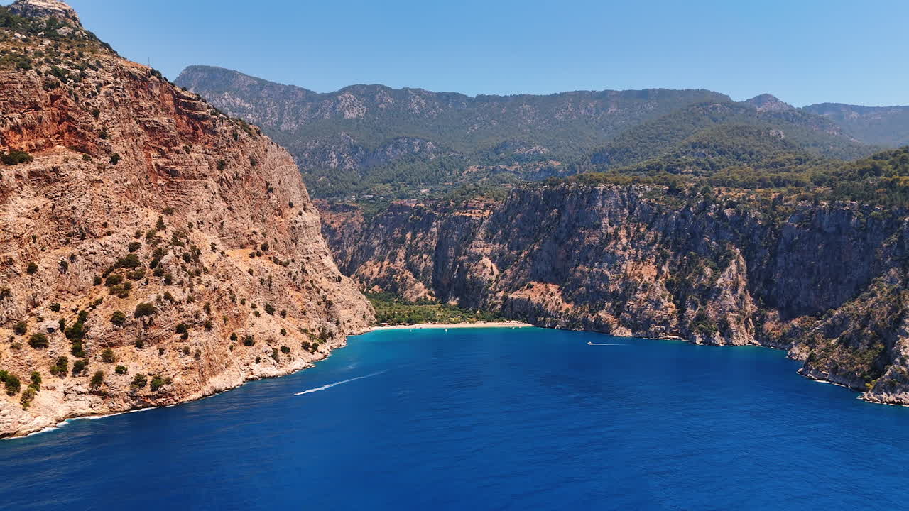 Spectacular rocks with poor vegetation on the slopes. Two boats move by the azure waterscape of the sea
