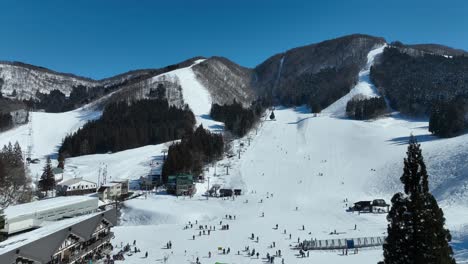 Aufsteigende-Mittlere-Aufnahme-Des-Unteren-Endes-Einer-Skipiste,-Skifahrer-Kommen-Am-Fuß-Des-Berges-An-Und-Stellen-Sich-Für-Die-Sessellifte-An