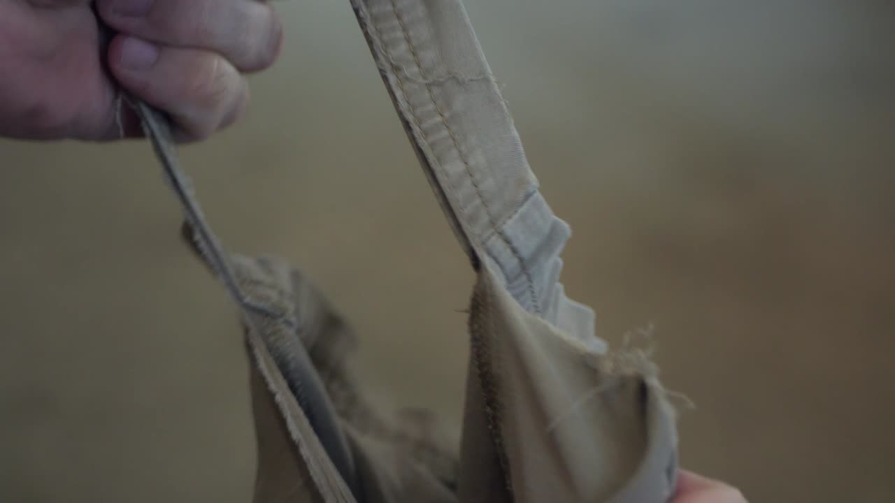 Close-up of a hand pulling apart worn fabric, revealing a ripped seam and frayed threads as the material tears. Useful for themes of damage, repair, textiles, and wear
