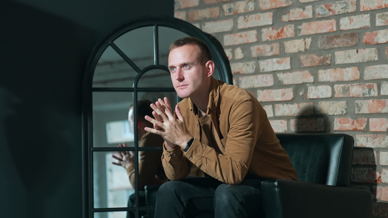 Thoughtful focused Caucasian man sitting in the armchair. Man feeling tired holds his head.