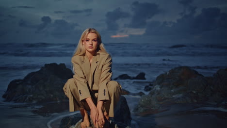 attractive model sitting rocks at evening ocean waves. fashion woman posing