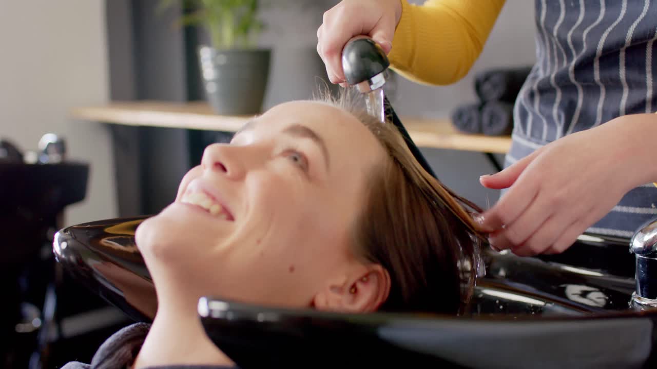 백인 여성 헤어드레스러의 손이 편안한 여성 고객의 머리를 고, 살롱에서 미소 짓고 있습니다.