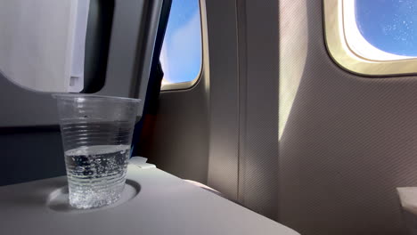 airplane tray table on seatback with clear fresh bubbly sparkling water in disposable cup