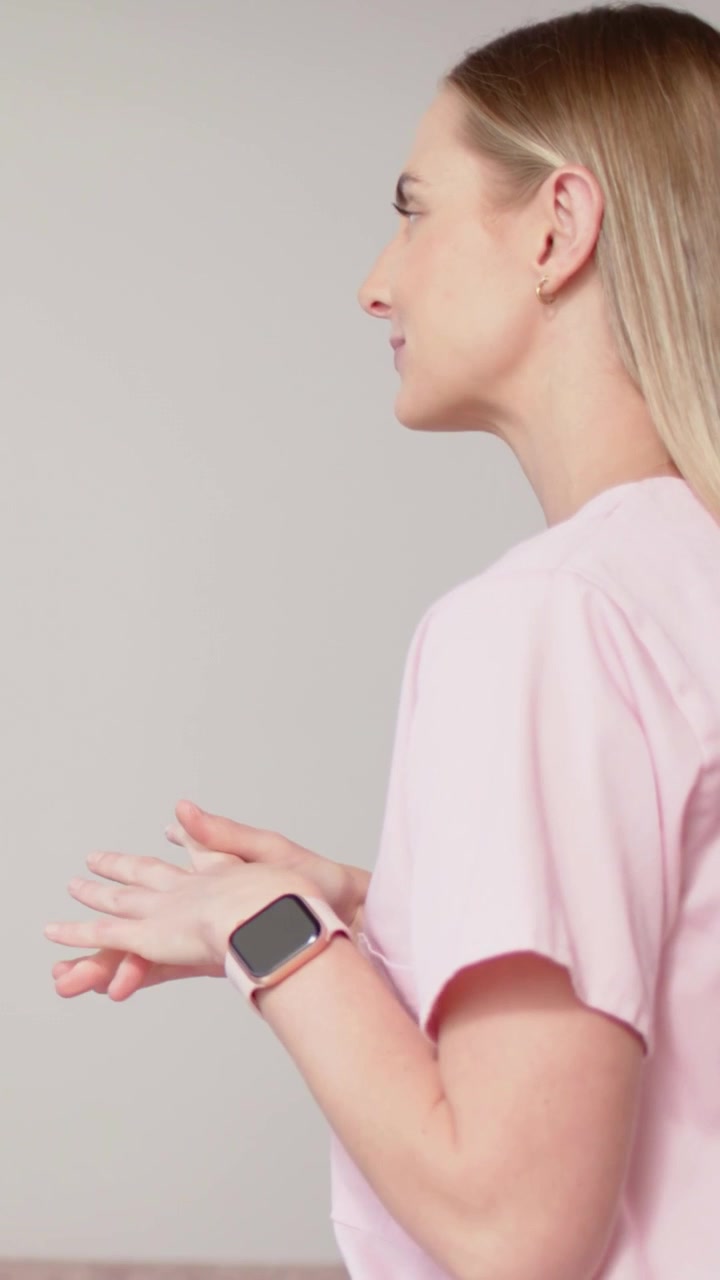 Video verticale: Donna che fa piccoli gesti mentre parla in studio, con orologio e top rosa, con spazio per il testo.