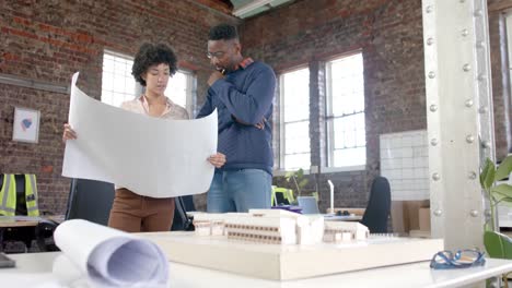 Diverse-architect-colleagues-discussing-work-with-building-model-and-blueprints-in-slow-motion