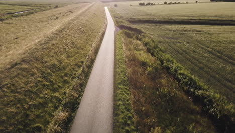 drone-is-heading-down-the-dyke-road-into-the-sun,-scenic-landscape,-sunset