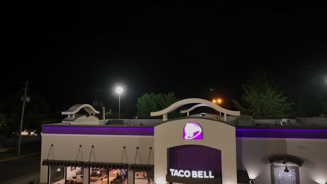 Taco Bell Restaurant lighting at night. Modern building in America with purple bell sign. Suburb district of Roanoke City, Virginia. Aerial rising shot.