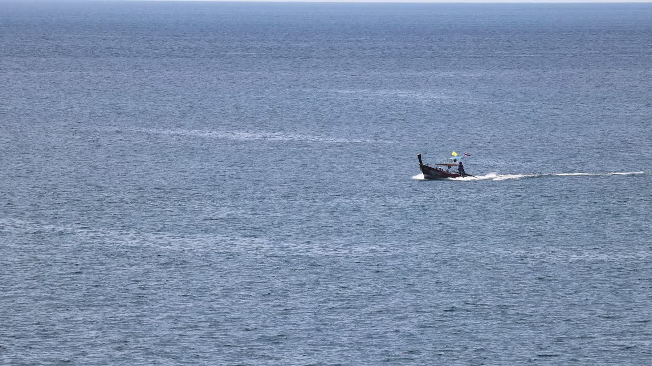 A longtail boat glides across the ocean near Phuket, Thailand, under clear skies, capturing serene maritime travel