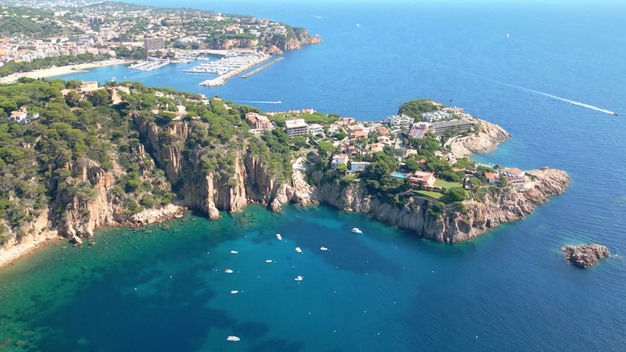 Amazing aerial perspective of the rugged coastline and clear turquoise water of sant feliu de guixols on the costa brava, showing luxury villas, boats, and the distant city marina