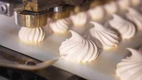 white creamy marshmallows are squeezed on the moving conveyor belt. close up. automated line for sweet products manufacturing. confectionery concept.