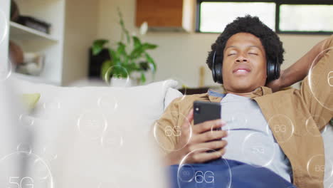relaxing on couch, man with headphones holding smartphone with 5g and 6g animations