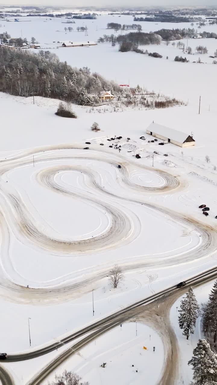 Vertical drone shot circling cars driving on a countryside ice track, winter day