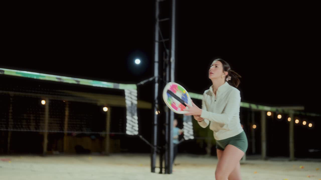 Woman Playing Beach Tennis at Night on a Sand Court
