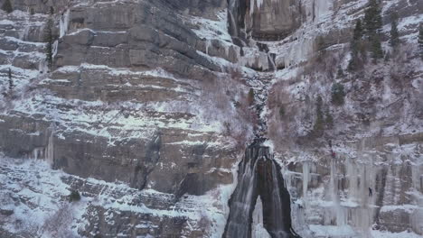 athletic ice climbers dangerously climb a frozen waterfall along a shear cliff - panning down