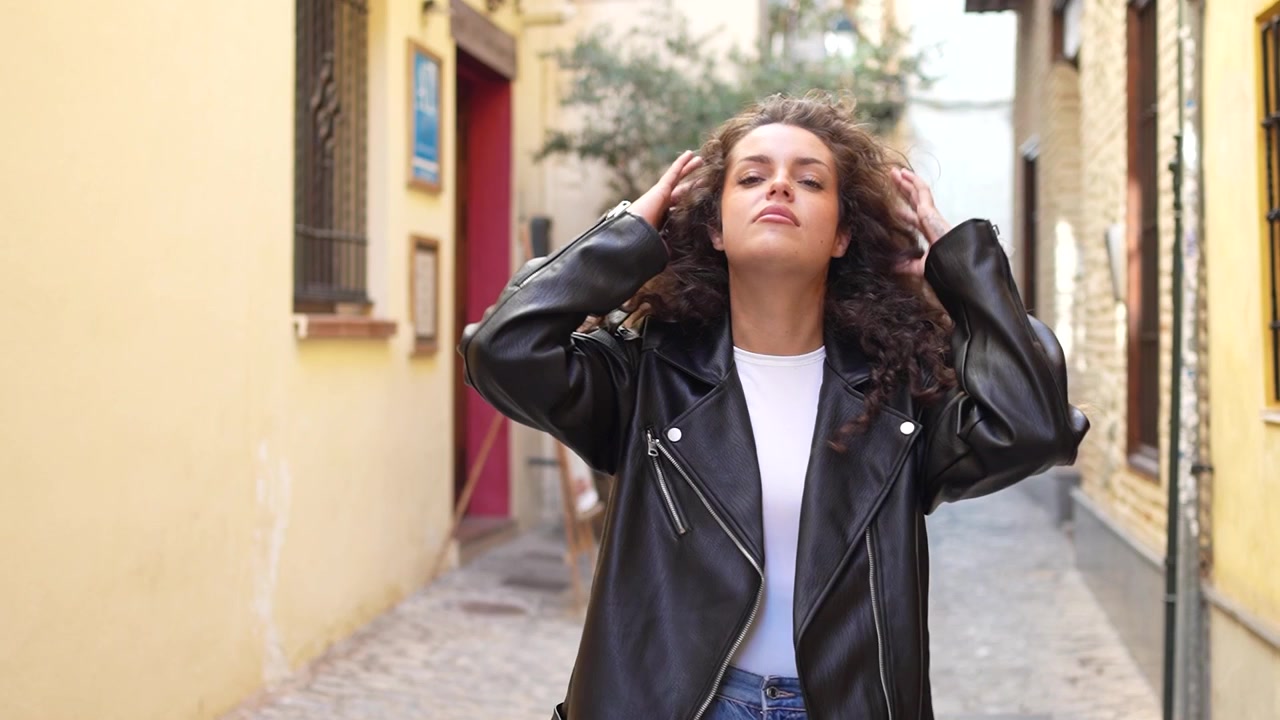 Una mujer elegante con hermoso cabello rizado se para con confianza en un callejón urbano.