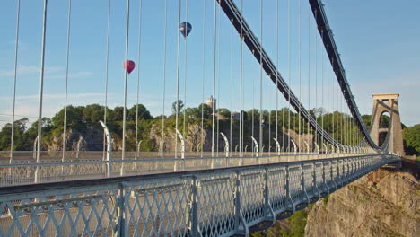Traffic-Drive-Across-Clifton-Suspension-Bridge-with-View-of-Hot-Air-Balloons-in-flight-over-Cabot-Tower-on-a-Sunny-Evening---horizontal-perspective