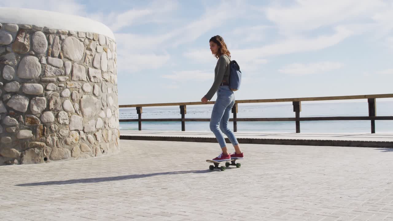 Happy mixed race woman skateboarding on sunny promenade by the sea