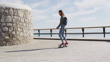 happy mixed race woman skateboarding on sunny promenade by the sea