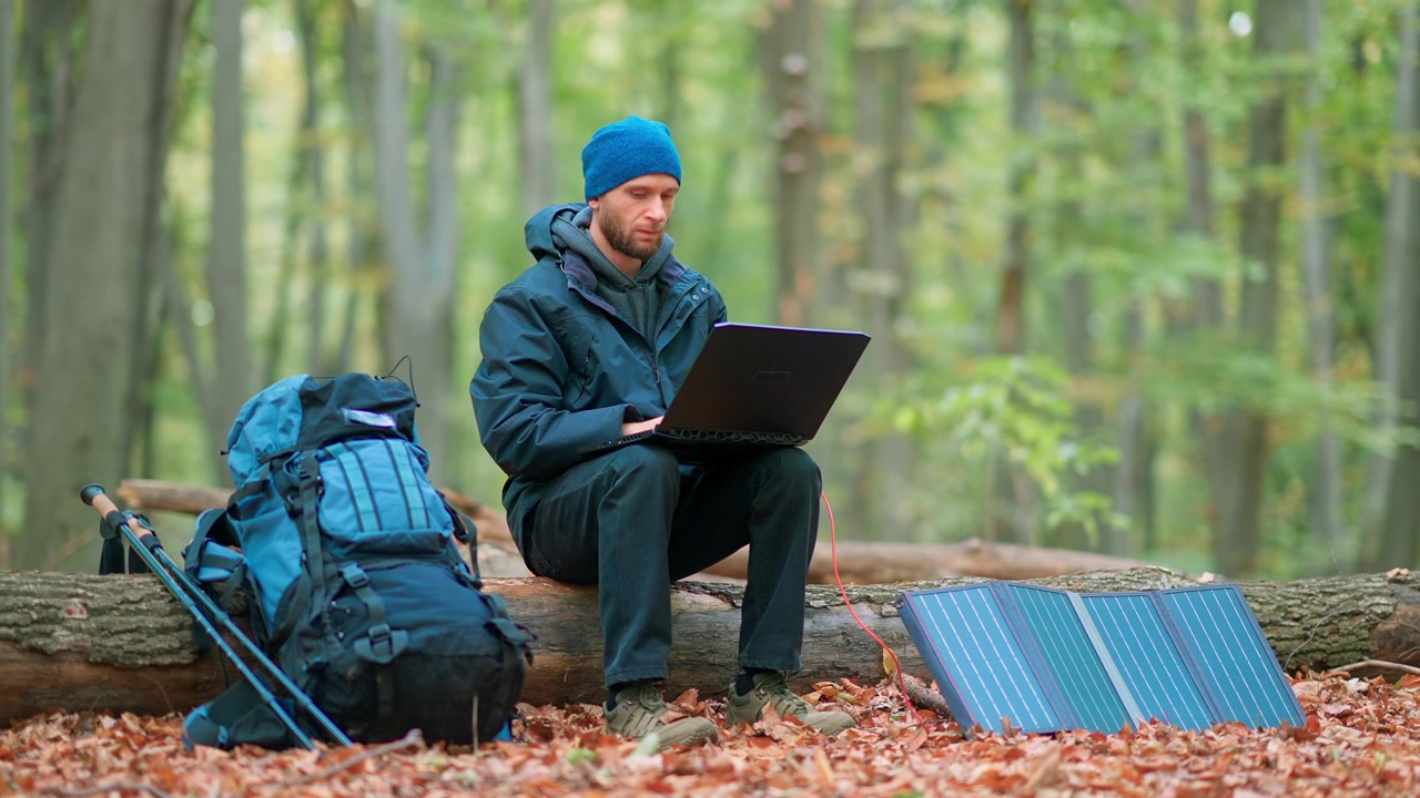 Man Working on Laptop in Forest, Powered by Solar Panel