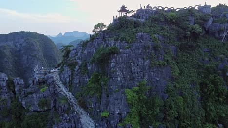 aerial view of stairs to viewpoint on cliff with dolly back over pagoda with tourists visiting at ninh binh in vietnam