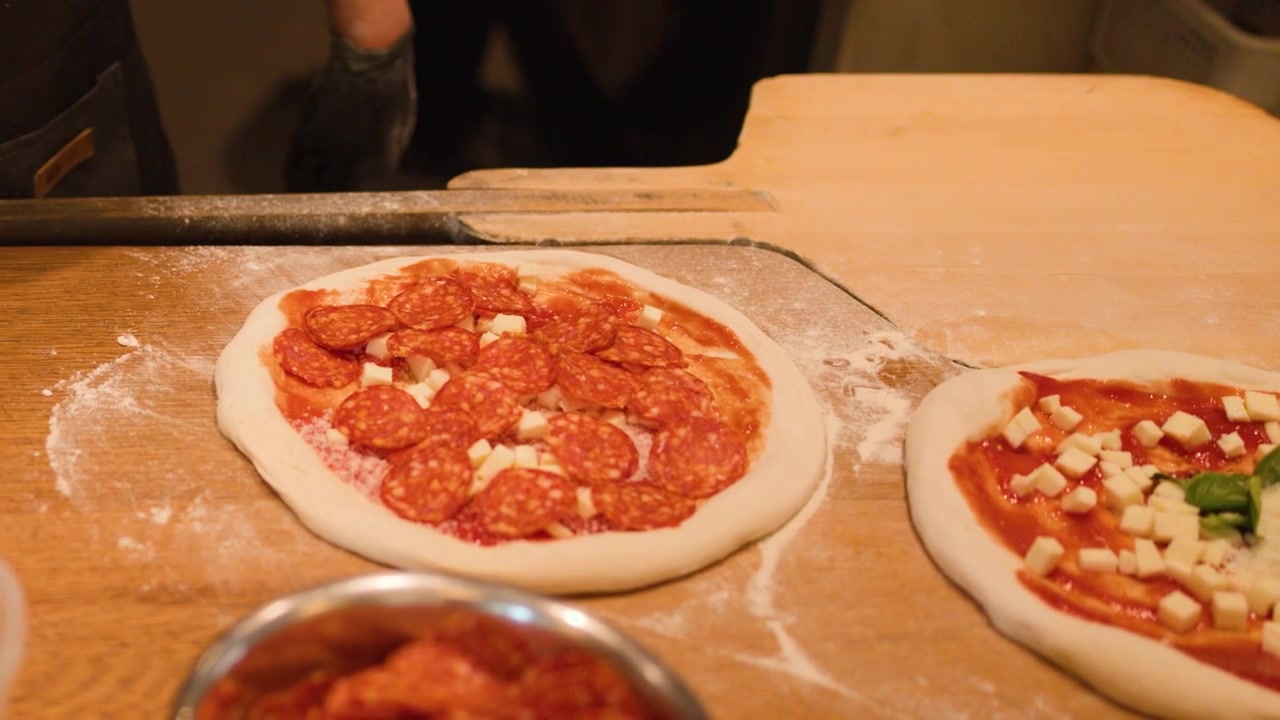 Primo piano di uno chef con guanti neri che mette il salame piccante sulla pizza in un ristorante.
