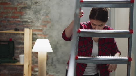 Woman-drops-down-brush-climbing-on-ladder-in-living-room