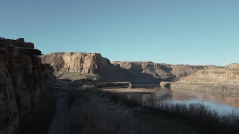 Scenery-of-a-desolate-landscape-in-Utah,-USA,-with-a-winding-road-near-a-flowing-river-and-majestic-hills-in-the-backdrop