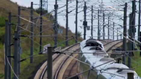 vista trasera de un tren eléctrico de pasajeros de alta velocidad que pasa por debajo de torres de energía eléctrica