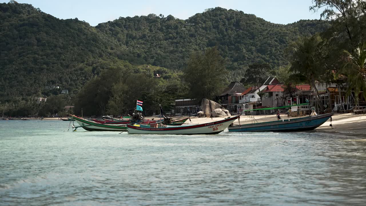 Empty longtail boats quietly moored in the shallow waters of Sairee Beach on Koh Tao, Thailand, surrounded by lush greenery and coastal scenery.