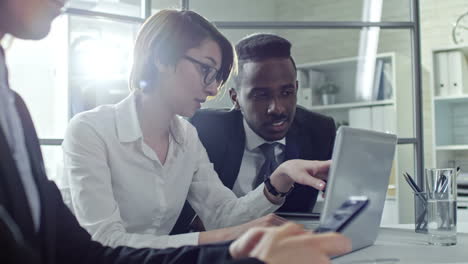 Young-Businesswoman-And-Businessman-Discussing-Presentation-On-Laptop-Screen-While-Female-Colleague-Texting-On-Smartphone