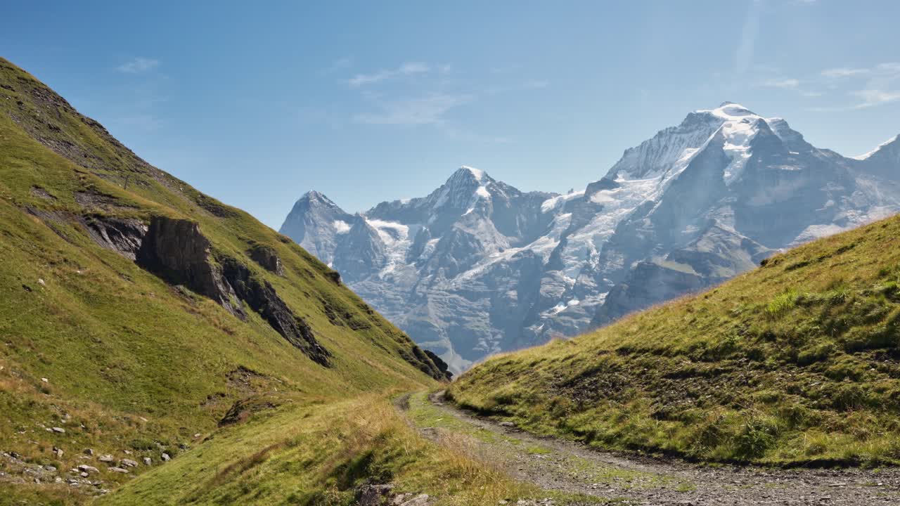 관광객은 잔디로 인 계곡의 도로의 이미지를 포착했고, 배경에는 눈으로 인 산들이 있습니다.