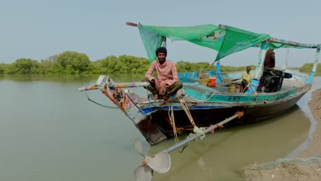 aerial pan shot of a pakistani man glancing at the camera while sitting on local boat in the indus river delta mangrove near karachi.
