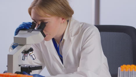 female lab worker researching omicron variant of covid-19 and possible vaccine with microscope