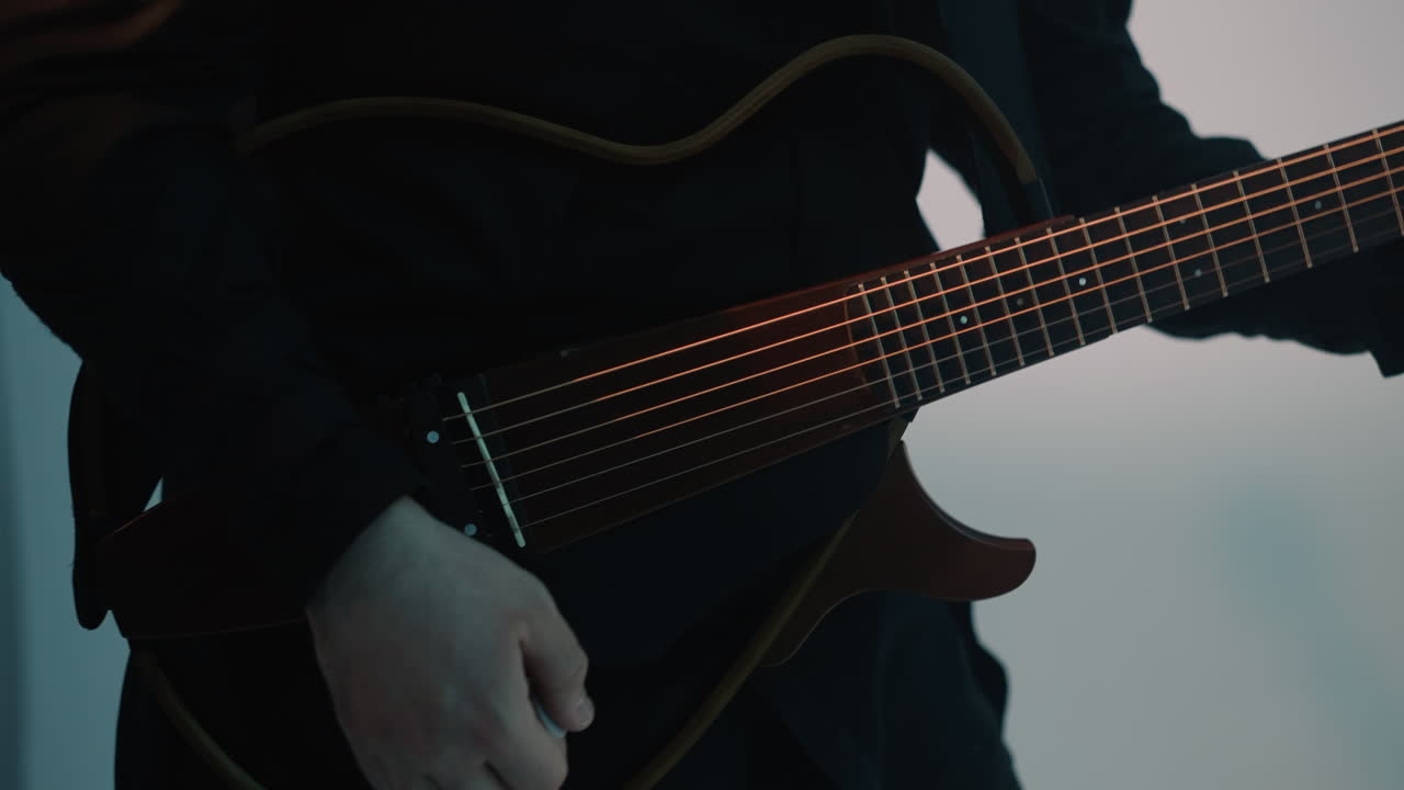 Faceless guitarist in a black shirt playing guitar against a grey background. The close-up captures the intricate details of the guitar and the musician's hands