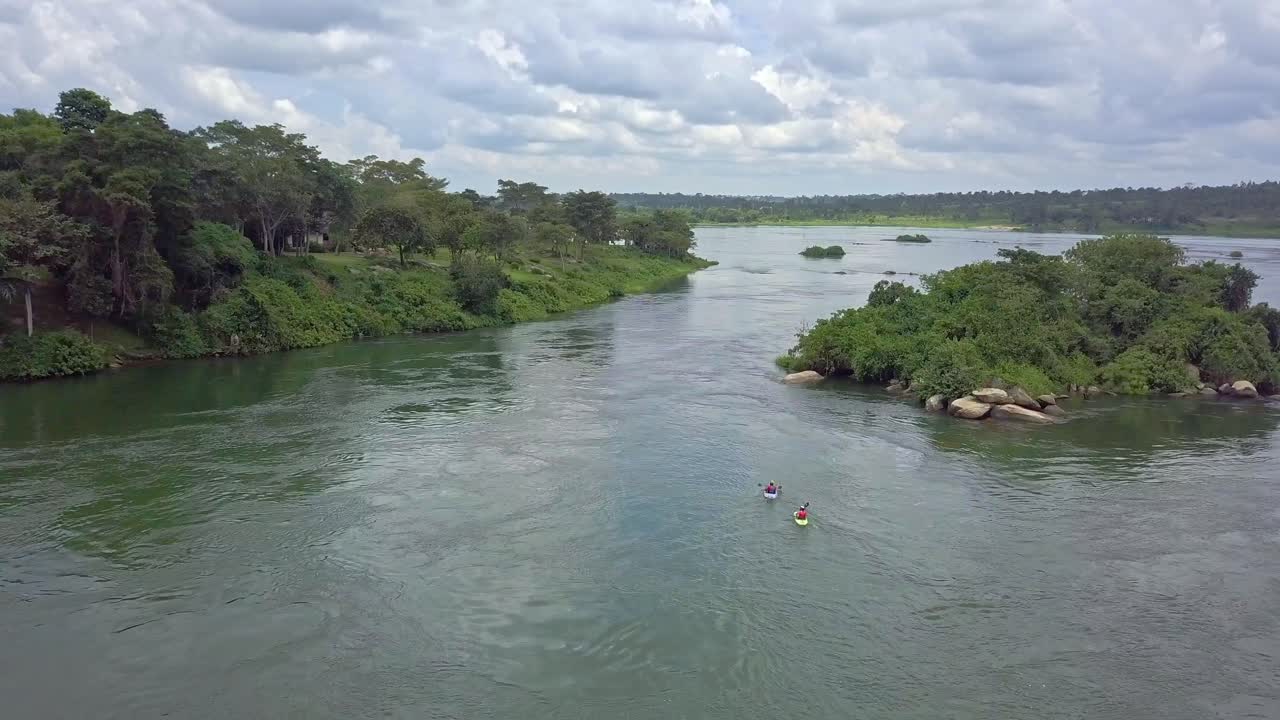 Aerial view of kayakers paddling on the River Nile in Uganda, Africa, surrounded by lush green riverbanks, forested edges, and partly cloudy skies