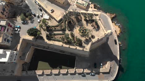 Aerial-shot-over-an-old-city-surrounded-with-sea-and-down-towards-a-garden