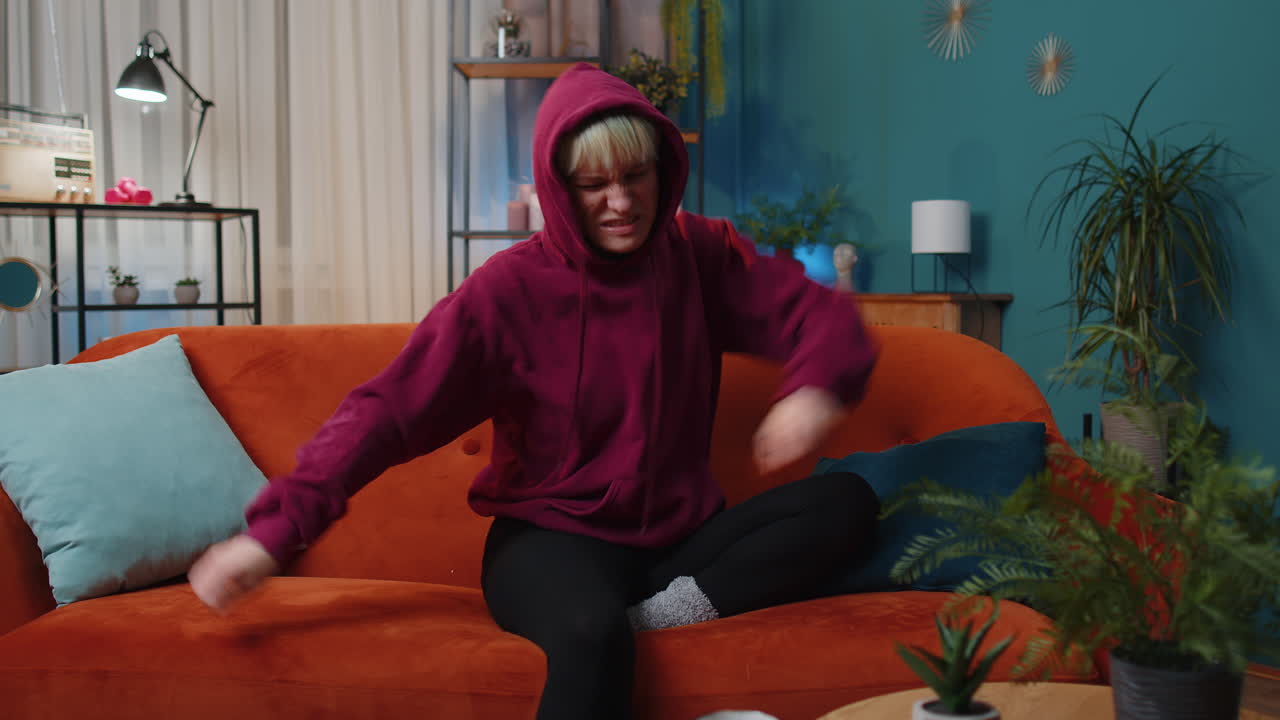 Trendy cheerful woman dancing and moving to rhythm making dub dance gesture at modern home