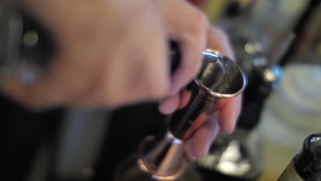 pouring liquor into metal measure glass to prepare alcohol cocktail, close up