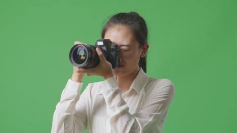 스튜디오에서 녹색 스크린 배경에 서서 몇 장의 사진을 찍는 카메라를 사용한 후 시도 된 아시아 사진작가의 클로즈업