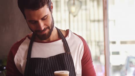 Smiling-waiter-holding-coffee-at-counter-in-cafe